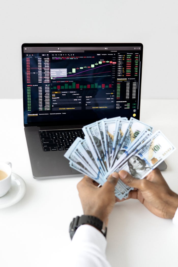 Hands holding cash in front of a laptop displaying stock market data, symbolizing financial growth and investment.